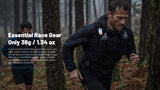 A man running through a misty forest wearing a black waterproof jacket with a hydration pack and a small white electronic whistle on the chest. White text on the left reads 'Essential Race Gear Only 38g / 1.34oz